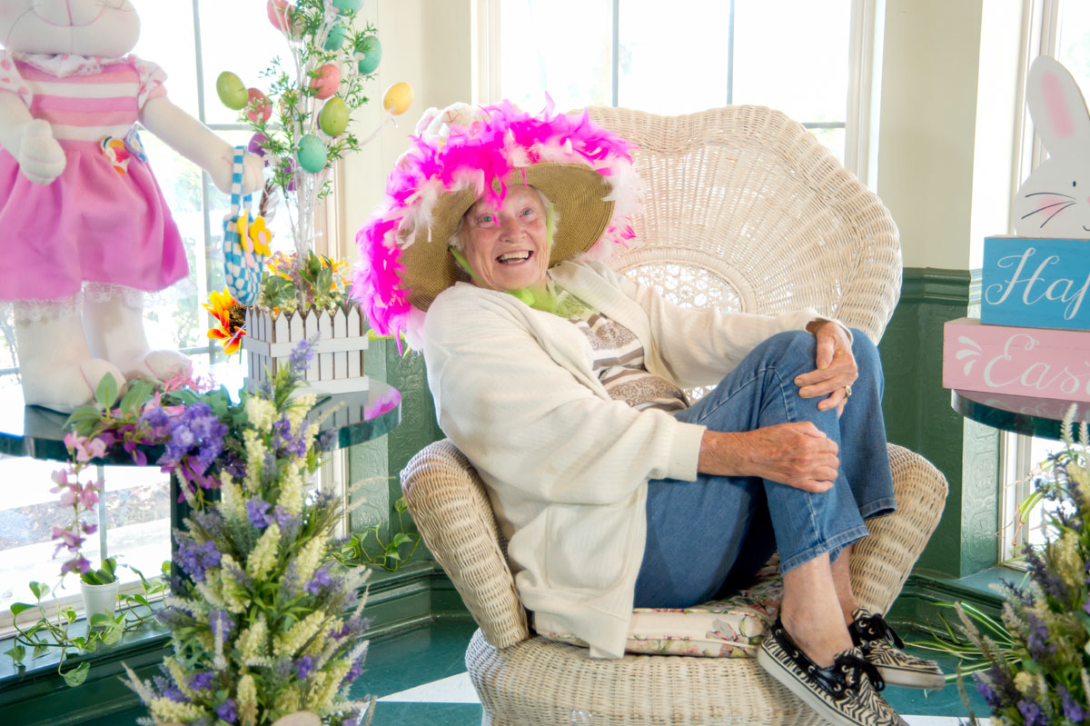 Elderly woman wearing a fun easter hat in a sunlit assisted living room chair in Metairie Kenner New Orleans assisted living facility