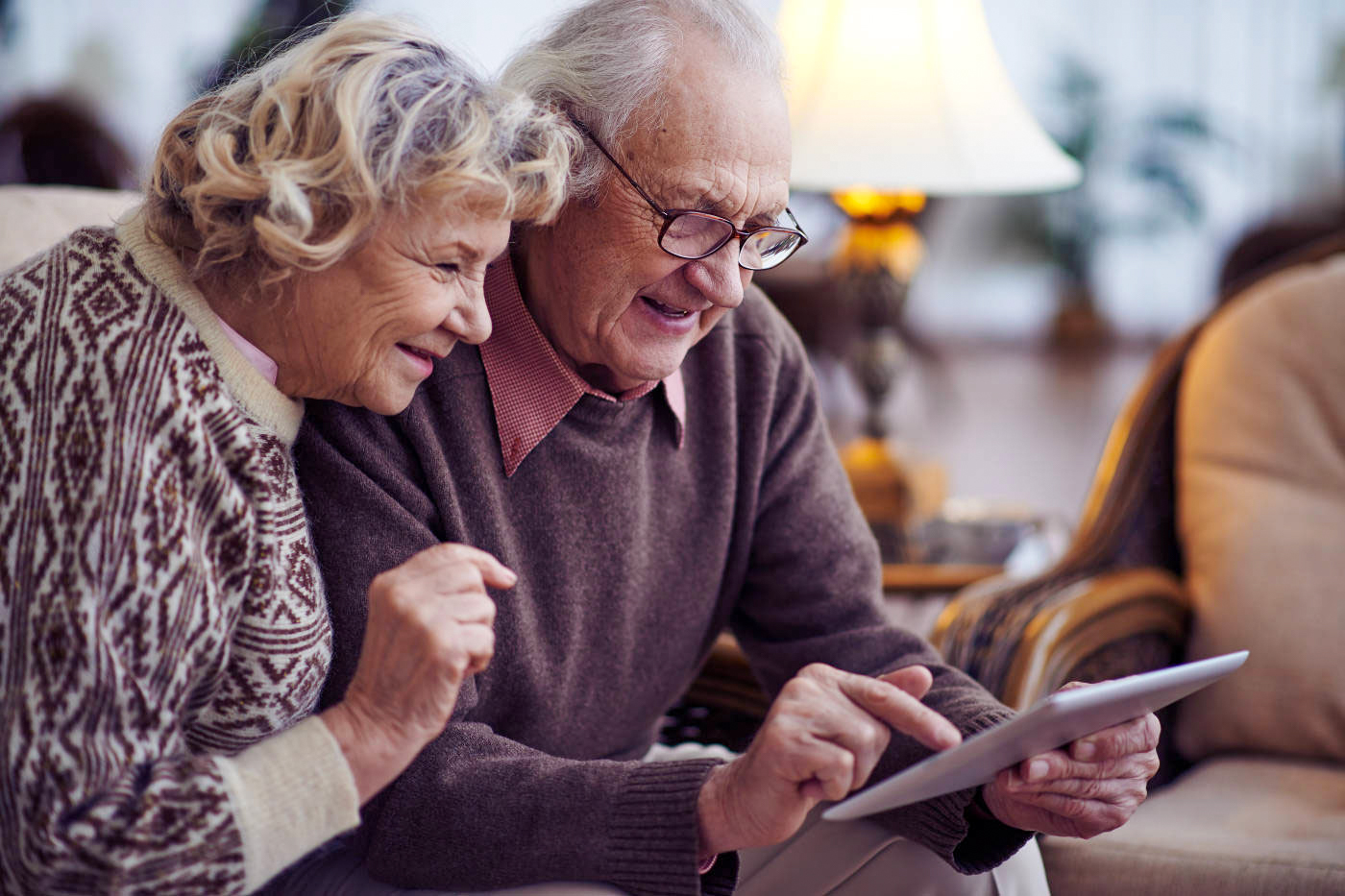 elderly couple sitting on sofa in living room looking at tablet