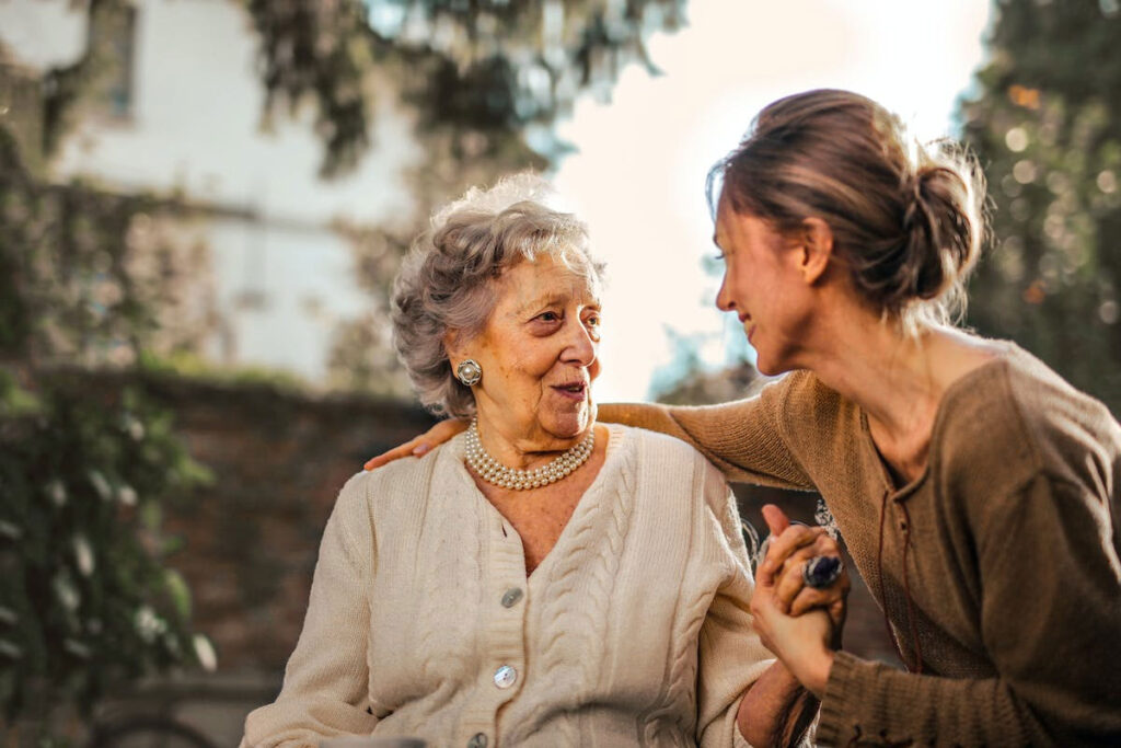 In the soft glow of the afternoon sun, a concerned middle-aged woman gently discusses recent falls and the possibility of transitioning to assisted living in Metairie with her elderly mother, their thoughtful conversation unfolding amidst the tranquility of their shared outdoor space.